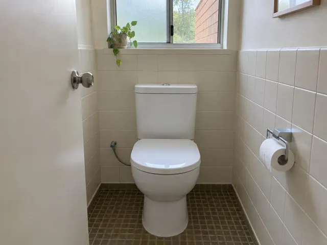 Clean white toilet in a tiled bathroom with a small window and tiled floor in Curl Curl