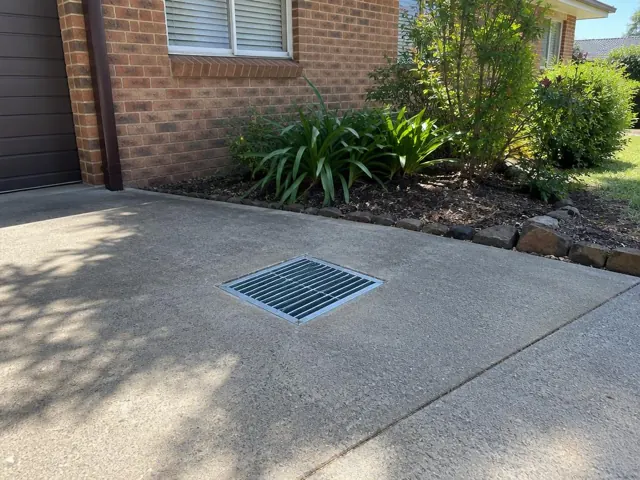 Driveway stormwater grate set flush beside brick house and garden in Beacon Hill